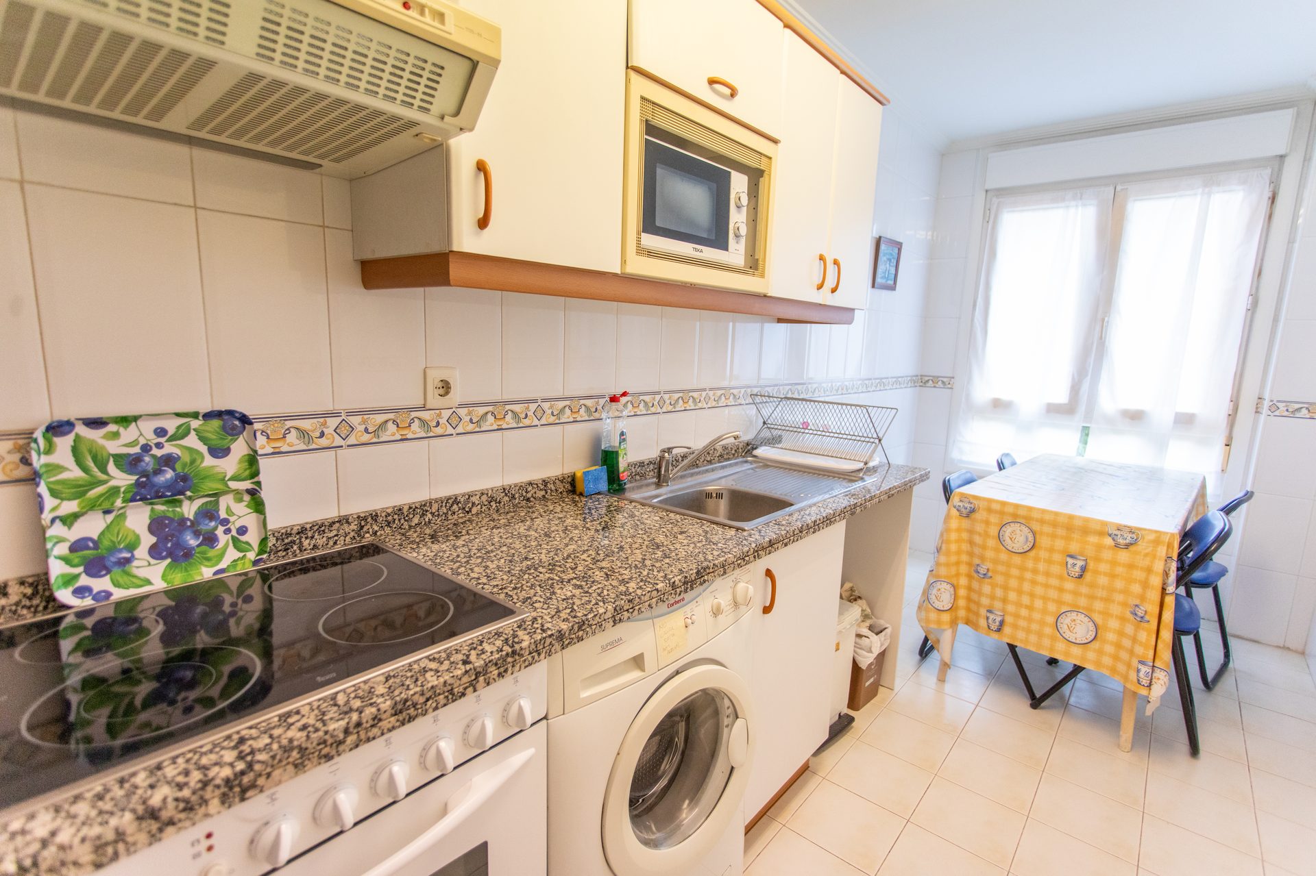 Cocina con vitrocerámica, lavadora y mesa junto a la ventana